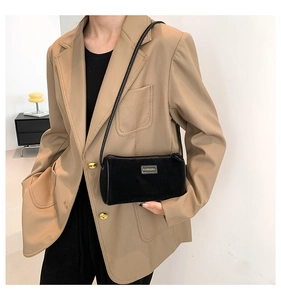 Dettaglio di una borsa a tracolla in camoscio nero indossata con un blazer color cammello