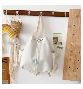 Detailed close-up of a beige nylon drawstring bucket bag hanging on a dark wood rack