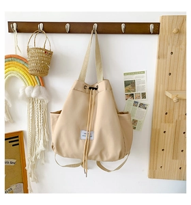 Detail of drawstring opening and fabric label on beige nylon versatile backpack bag