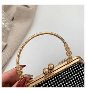 Detail of glittery black evening bag with gold floral embossed ring handle and rhinestones