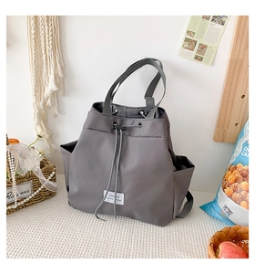 Detail of grey nylon drawstring tote bag featuring side pockets and a fashion woven label
