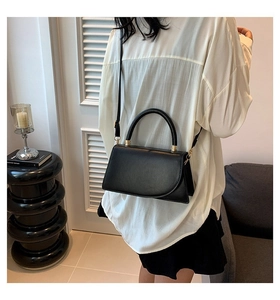 Detailed view of a black leather crossbody bag with curved flap and metal hooks