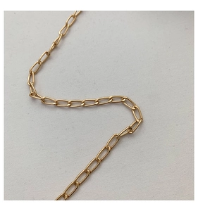 Close-up of golden paperclip chain with polished rectangular links on white fabric