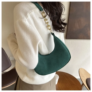 Side view of dark green crescent bag with gold chain strap on a white knit sweater