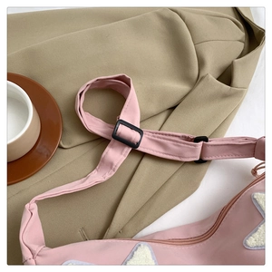 Detail of pink nylon crossbody bag with white star patch and adjustable strap buckle