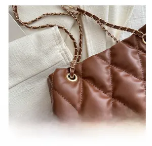 Detail van bruine gewatteerde emmertas met gouden oogjes en een leren ketting