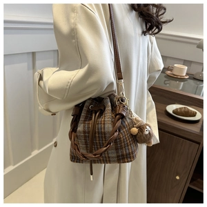 Detail of plaid drawstring bucket bag with plush monster charm and woven handle