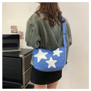 Detail of blue nylon crossbody bag featuring three white plush star appliques and wide strap