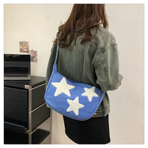 Blue nylon crossbody bag with white plush star patches worn by model in casual setting