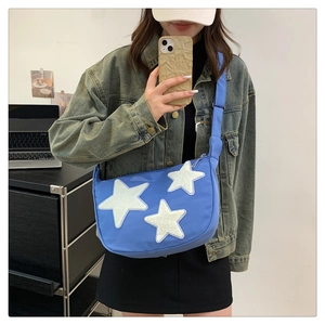 Blue nylon crossbody bag featuring white star patches and adjustable wide strap detail
