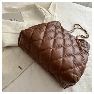 Detail van bruine gewatteerde bucket bag met kettingriem op een zachte linnen achtergrond