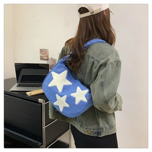 Blue nylon crescent bag featuring white plush star patches worn by a model in casual setting
