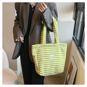 Dettaglio della borsa tote in peluche a righe gialle e blu con patch logo indossata
