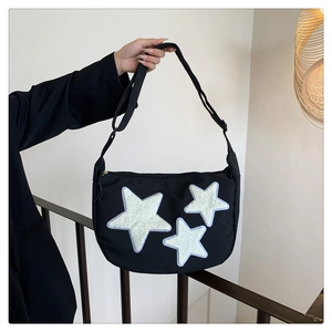 Detail of black crescent crossbody bag with white plush stars and adjustable strap