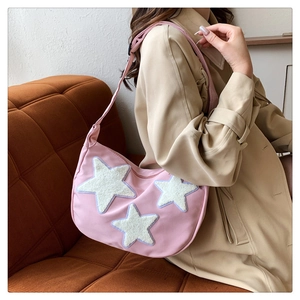 Detail of pink nylon half-moon bag featuring three white plush star patches and adjustable strap