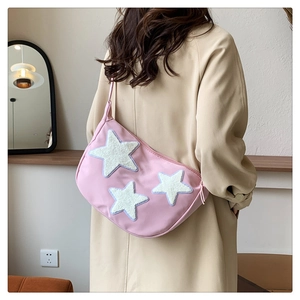 Pink crescent nylon bag with plush star patches shown on model in cozy indoor setting