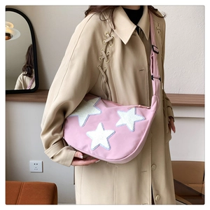 Close-up of pink nylon crescent bag featuring white plush star patches and adjustable strap