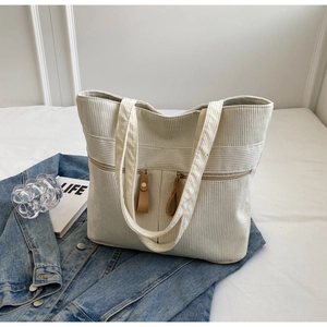 Detail of white corduroy tote bag featuring dual front pockets with brown leather zipper pulls