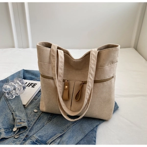 Detail of corduroy tote bag featuring vertical stripes and dual front zipper pockets