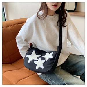 Detailed view of black nylon crossbody bag featuring white plush star patches on the front