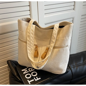 Detailed view of beige corduroy tote bag featuring dual front zipper pockets on leather sofa