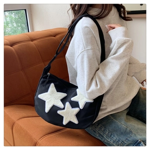 Detail of black nylon crescent bag featuring plush star patches on a casual outfit