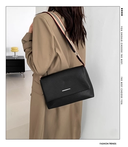 Détail d'un sac bandoulière en cuir noir avec sangle rayée et boucle métallique élégante