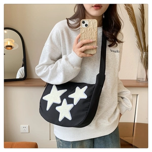 Close-up of black nylon crossbody bag with white plush stars and wide strap detail