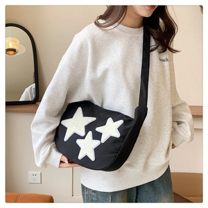 Detail of a black nylon crossbody bag featuring three white star patches on a model