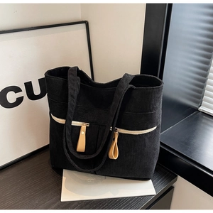 Detail view of black corduroy tote bag with front zipper pocket on a wooden surface