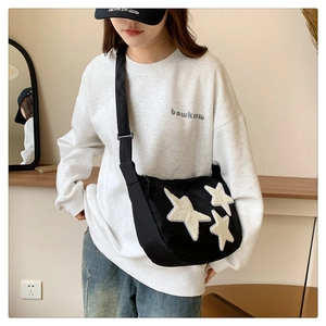 Detail of black nylon crossbody bag featuring three plush star patches and wide strap