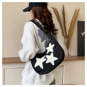 Detail of black nylon crescent crossbody bag with white plush stars on a female model