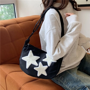 Black crescent nylon crossbody bag with white plush stars shown on a shoulder