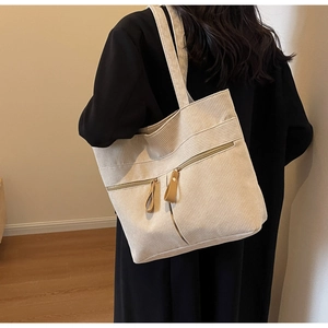 Detail of beige corduroy tote bag showing soft ribbed texture and brown leather zipper pull