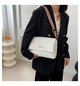Détail du sac bandoulière blanc grainé avec une sangle en toile rayée sur blazer noir