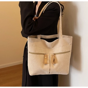 Detail view of beige corduroy tote bag with dual front zipper pockets on a black blazer