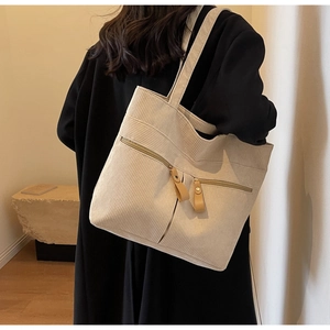Detail of beige corduroy tote bag showing ribbed texture and zipper pocket on shoulder