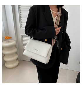 Détail du sac à bandoulière crème minimaliste avec une large bandoulière rayée et rabat