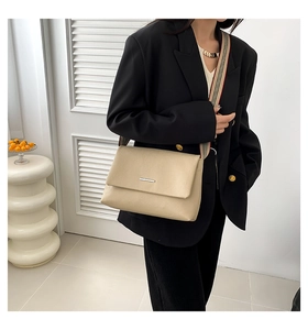 Détail du sac beige en cuir grainé avec barre métallique et bandoulière rayée