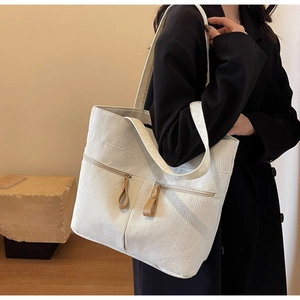 Model wearing a large cream corduroy tote bag with double zipper front pockets