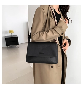 Détail d'un sac bandoulière en cuir noir avec une bandoulière textile à rayures colorées