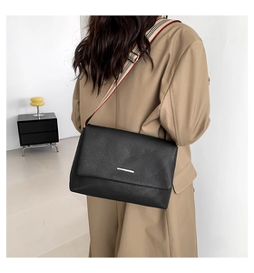 Détail du sac bandoulière noir grainé avec une large sangle en tissu rayé très élégante