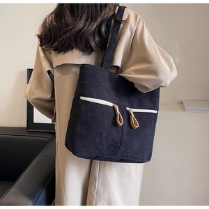 Detail of black corduroy tote bag showing dual zipper front pockets and textured material