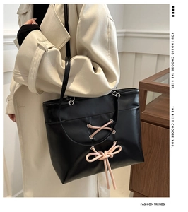 Detail view of black leather tote bag with pink drawstring bow decoration on female model