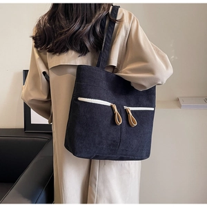 Detail of black corduroy tote bag featuring dual front zipper pockets and leather pullers