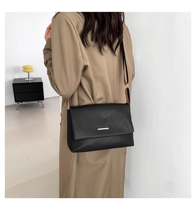 Détail du sac bandoulière en cuir noir avec sangle rayée et garniture argentée