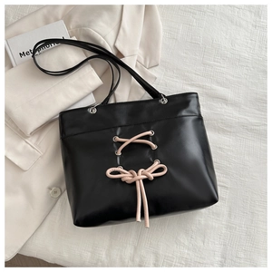 Detail of black leather tote bag featuring a pink drawstring bow and metal eyelets decoration