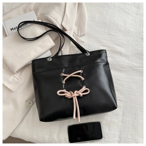 Detail of black leather tote bag featuring pink lace-up bow and silver metal eyelets