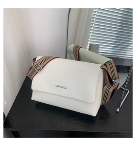 Détail d'un sac à main blanc en cuir grainé avec bandoulière rayée sur bois noir