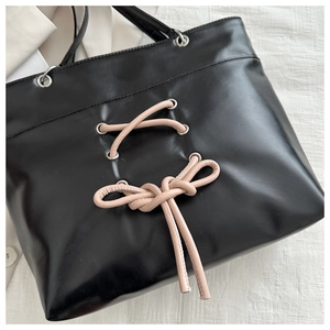 Detail of black leather tote bag featuring a pink bow tie and silver metal eyelets